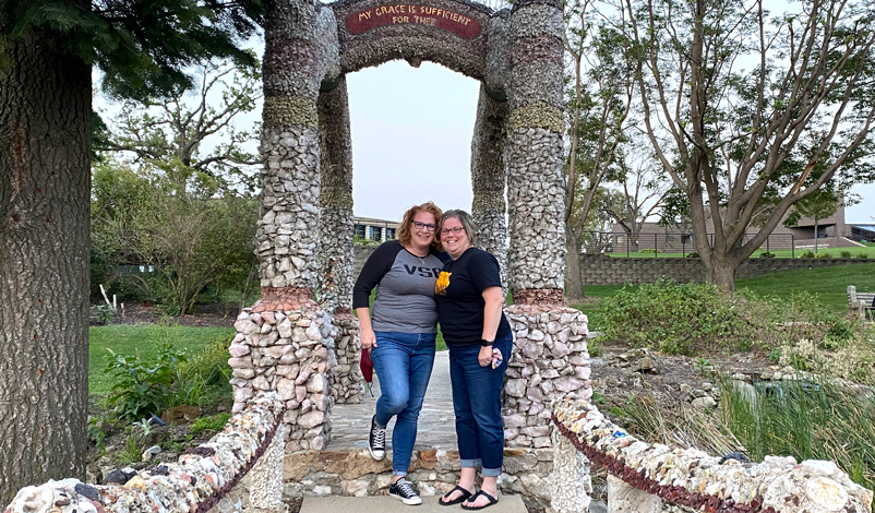 Kim Smith and Catherine standing beside the grotto in the greenspace in Mount Mercy University