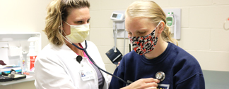 Nursing student practicing how to check the heart rate on another student.