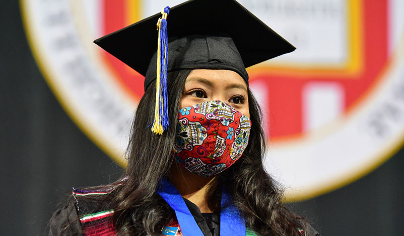 Alma standing in front of the university crest at her graduation ceremony