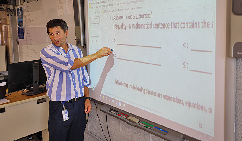 Terry standing in front of a projector, pointing at a math problem on the board