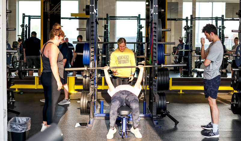 woman lifting bellbars with three coaches