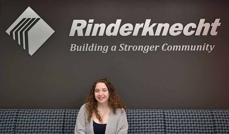 Faith posing in front of a sign for Rindeknecht Associates in Cedar Rapids