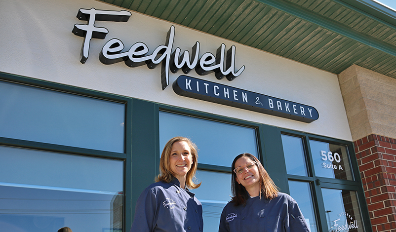 Melanie and Holly, standing in front of the Feedwell sign on their building