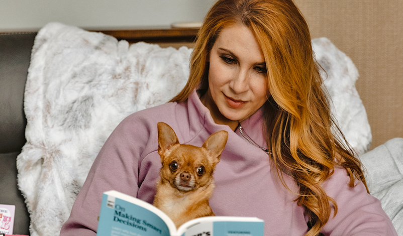 Feryl, sitting down and reading "Making Smart Decisions" with her chihuahua Cooper in her lap