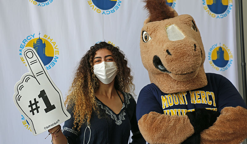 A student posing withh a #1 sign and Mount Mercy's mascot, Mustang Sally