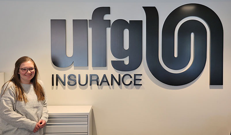 Jillian posing in front of a sign for UFG Insurance