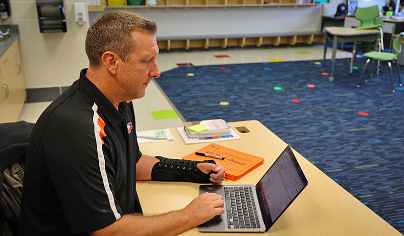 Brad sitting at a table in a classroom, looking at his laptop