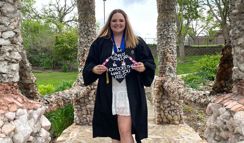 Macey in her graduation gown under the grotto