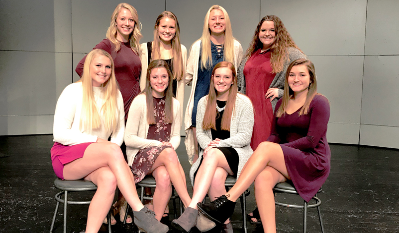 macey posing with a group of girls sitting in chairs in the McAuley auditorium