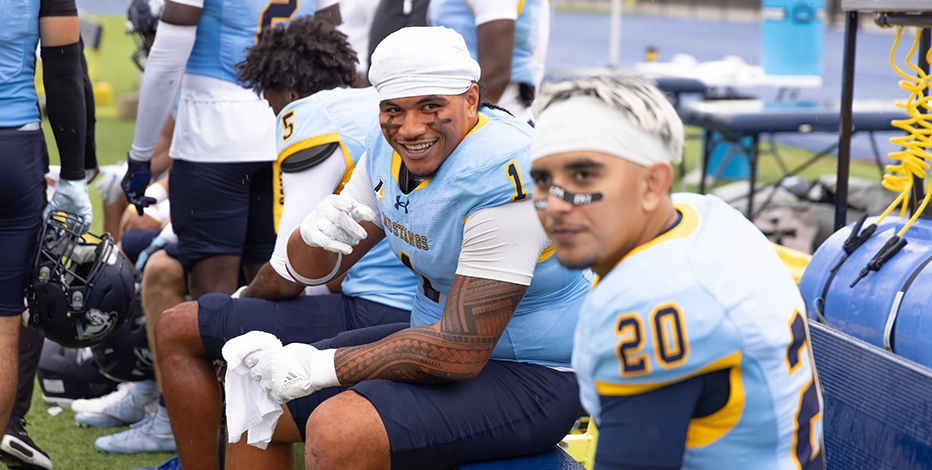 Two mount mercy football players smiling on the sidelines in their uniforms