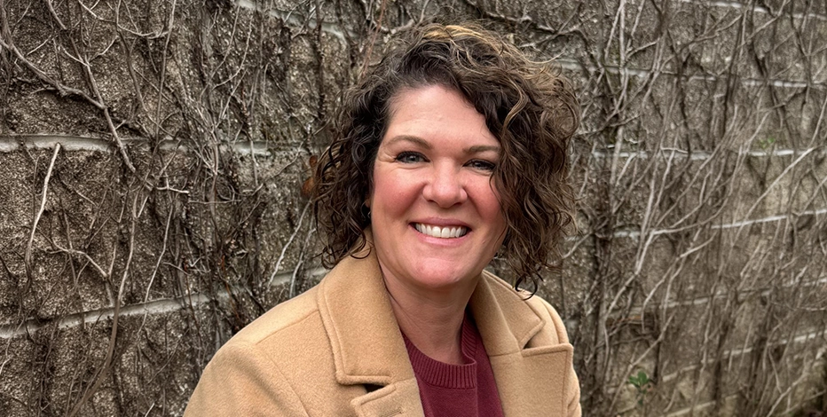Nicole Sakraida, M.Ed, smiles into the camera against a brick background.