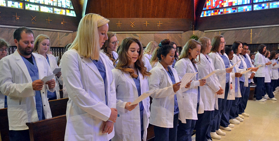Nursing students standing in the chapel, reading after receiving their white coats