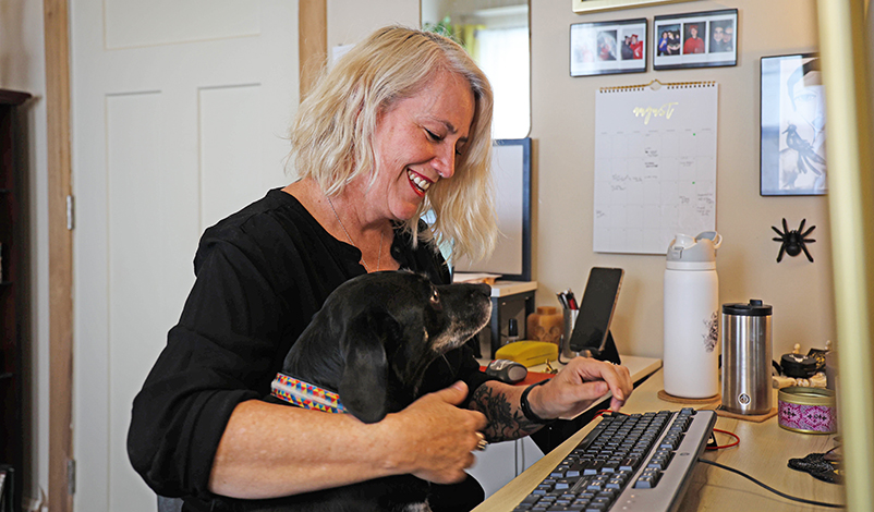 Jennifer working from home, hugging her dog with one arm and typing with the other
